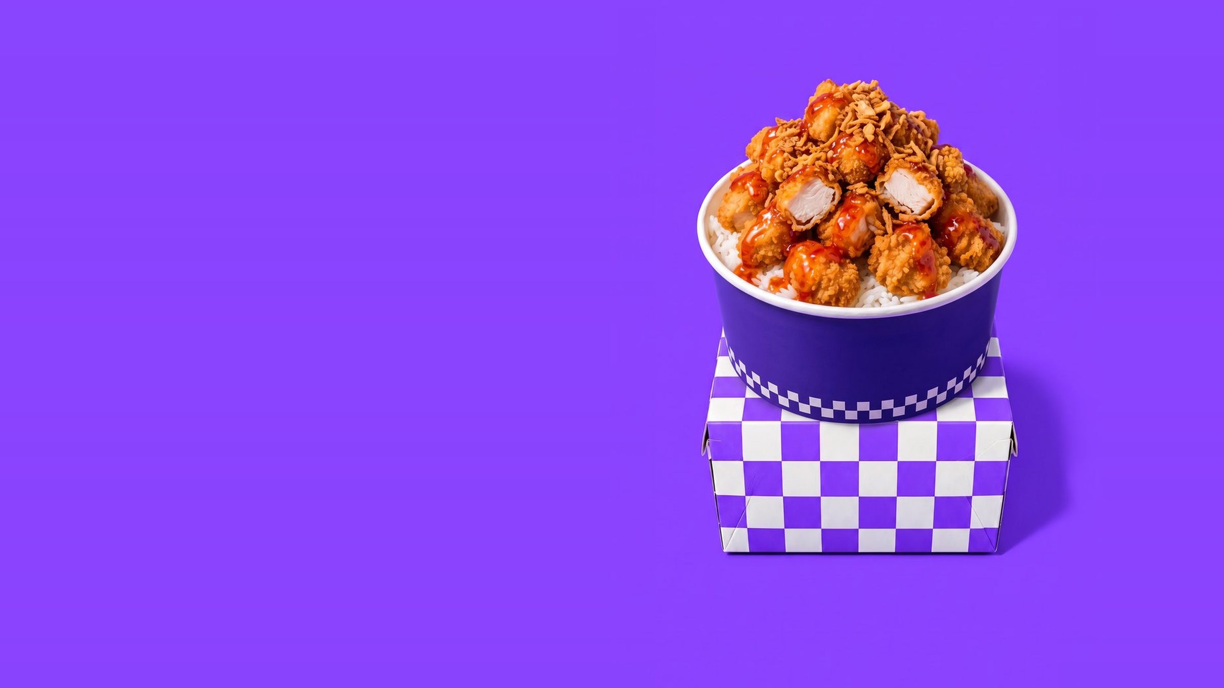 Bol de riz au poulet pané croustillant nappé de sauce devant un damier violet et noir